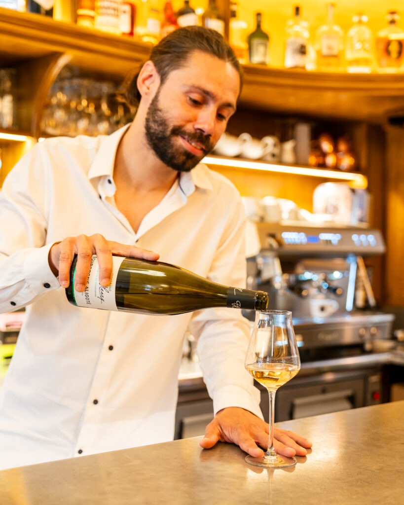 Un serveur verse, avec un air sympathique, une bouteille dans un verre à pied pour le servir au client 