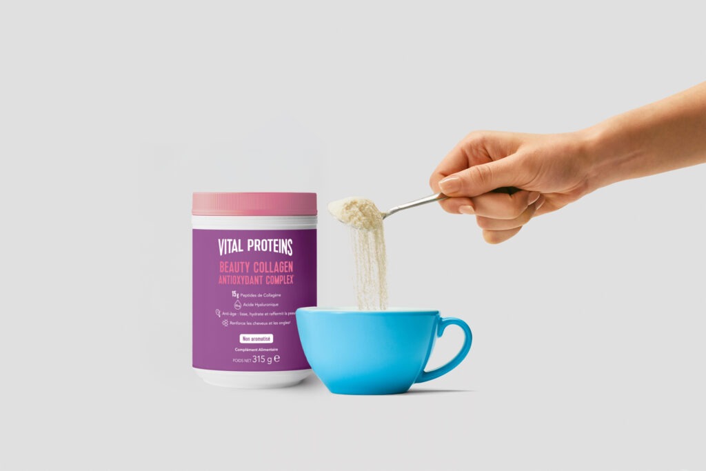 Main qui verse une cuillère de produit de Vital Proteins dans une tasse bleue