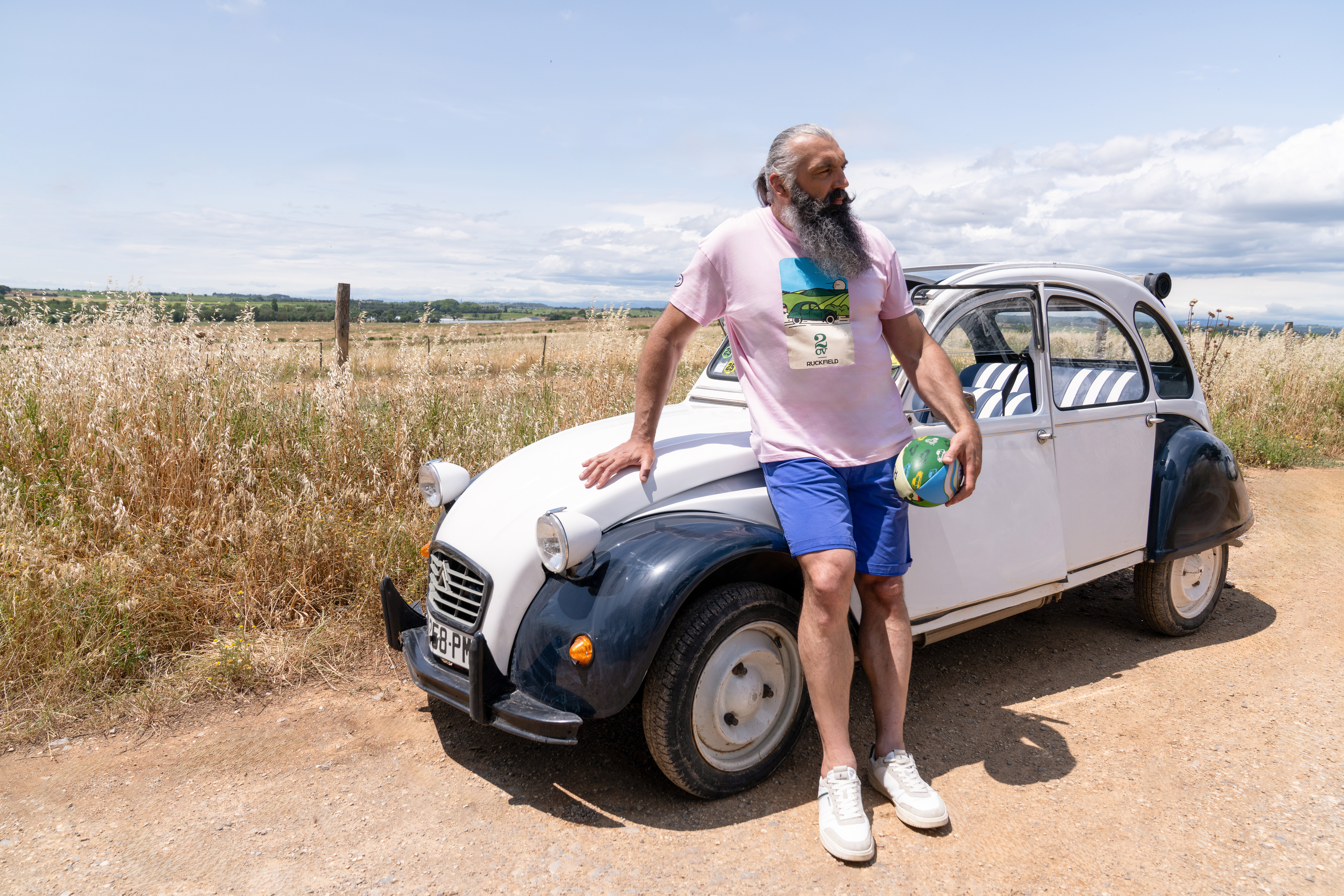 pub Ruckfield x 2CV avec un homme qui s'appuie sur le capot d'une 2CV