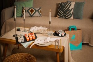 intérieur sobre, table garni de sushi evec deux bougies, à côté un sac de livraison de Deliveroo, une sorte de Date Night
